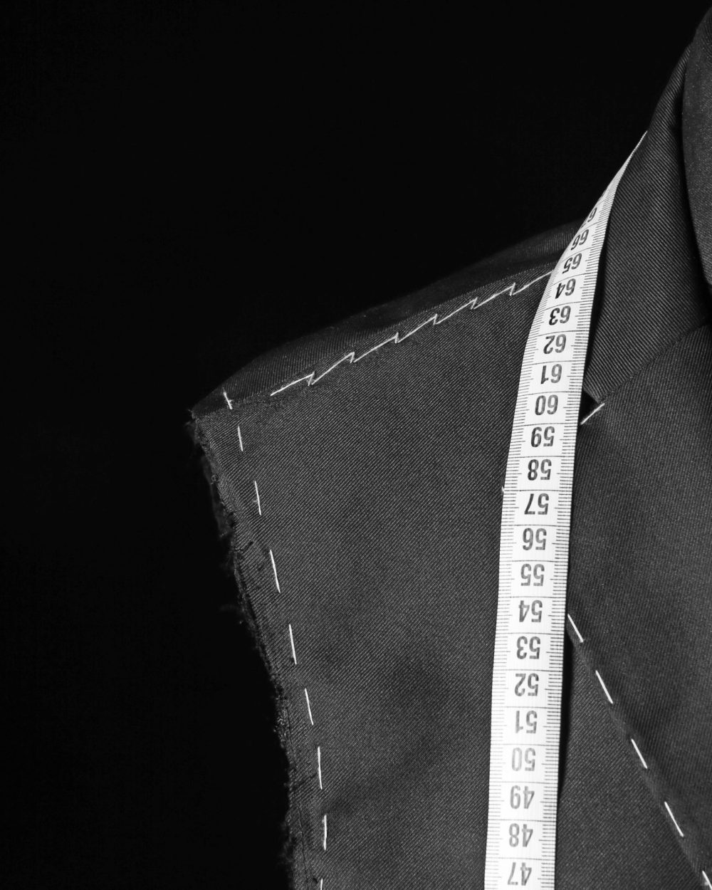 Tailor's mannequin with unfinished clothes and measuring tape on dark background, closeup